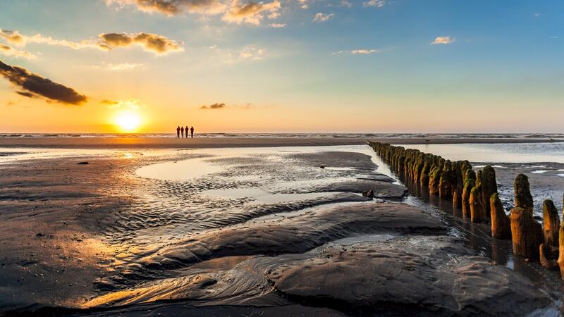 Sunset over mudlfats with a small group of people on the horizon and a pole fence on the right. © Janis Meyer/Waddenagenda.