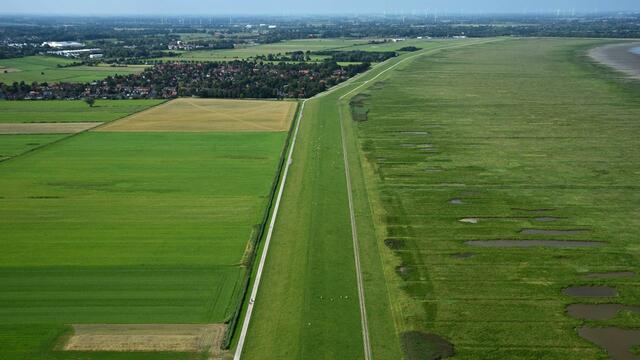 Aerial image of a straight dike line with fields and settlements on left and saltmarsh on right. © NLPV/Gregor Scheiffarth.